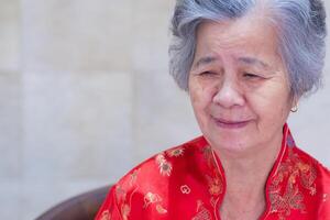 un mayor asiático mujer vistiendo un tradicional cheongsam qipao vestido, sonriente mientras en pie a hogar. chino mujer en rojo disfraz nuevo año celebracion. concepto de Envejecido personas chino y festival foto