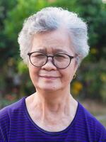 Portrait of an elderly Asian woman with short gray looking to the camera while standing in a garden. Space for text. Concept of aged people and healthcare photo