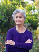 Elderly woman with short white hair standing smiling and arm crossed in the garden. Asian senior woman healthy and have positive thoughts on life make her happy every day. Health concept photo