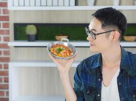 Young man wearing glasses sitting looking at the fried egg served on a pan with colorful toppings served on a pan. photo