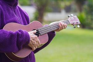 Close-up of hands senior woman holding ukulele while standing in a garden. Space for text. Concept of aged people and relaxation photo