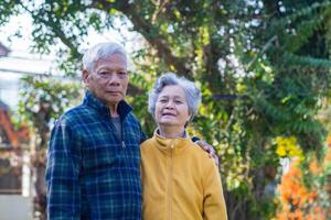 Portrait of an elderly couple with short gray hair, smiling and looking at the camera while standing in the garden. Concept of aged people, love, and healthcare photo