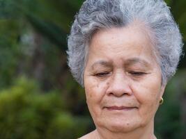 de cerca de frente a un mayor mujer sonriente y mirando abajo mientras en pie al aire libre. espacio para texto. concepto de Envejecido personas y cuidado de la salud foto