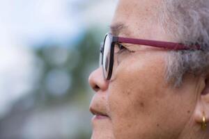 Side view of a senior woman wearing glasses and looking away while standing in a garden. Space for text. Concept of aged people and healthcare photo