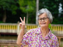 Portrait of happy senior woman hand showing victory sign, smiling, and looking at the camera. Concept of aged people and relaxation photo