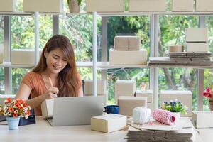 mujer de negocios sonriente y escribir datos en cubrir paquete o empaquetar caja para preparar enviar a un cliente mientras sentado en un silla en el oficina. concepto de negocio y comercio electrónico foto