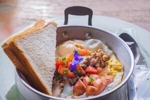 Close-up of fried eggs with bacon, hotdog, fresh tomato, and bread on a pan. Breakfast set photo