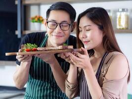 joven Pareja vistiendo delantal muy contento después Ayudar a hacer un filete a el cocina en su hogar, sonrisa y mirando el filete en un de madera plato. Pareja concepto foto