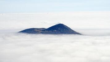 A lone mountain peak emerges above a dense sea of clouds under a clear sky photo
