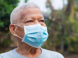 Senior man wearing a face mask and looking up while standing in a garden. Mask for protecting Covid-19, virus, coronavirus, pollen grains, etc. Concept of aged people and healthcare photo