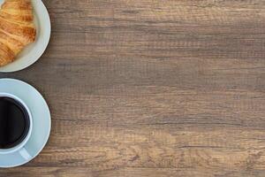 Top view of a white coffee cup and croissants on a white plate placed on a wooden table. Work from home. Space for text photo