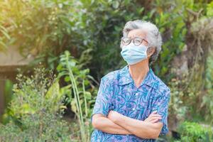 Portrait of a senior woman wearing a face mask and arms crossed while standing in a garden. Mask for protecting Covid-19, virus, coronavirus, etc. Concept of aged people and healthcare photo