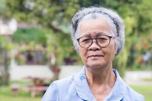 Senior woman with short gray hair smiling and looking at the camera while standing in the garden. Space for text. Concept of aged people and healthcare photo