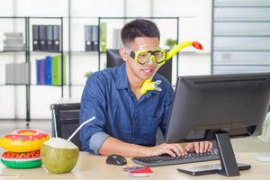 Young man wearing a diving mask yellow, smiling and sitting on a chair working in his office. He's a dream of the sea because the holiday coming soon. Holiday concept photo