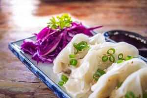 Side view of fresh Chinese dumplings or jiaozi on a plate on old wooden table. Selective focus. Chinese food with hot steams on an old wooden table photo