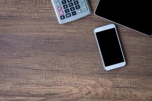 Top view of a tablet, calculator, and smartphone on a wooden table. Space for text. Wood texture background. Business and technology concept photo