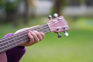 Close-up of hands senior woman holding ukulele while standing in a garden. Space for text. Concept of aged people and relaxation photo