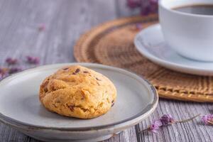 Close-up of a cookie on a plate with a white coffee cup and flower blurred background. Space for text photo