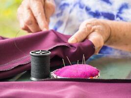 Close-up of hands senior woman's trying to thread a needle for sewing cloth. Space for text. Concept of aged people and relaxation photo