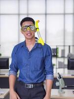 Portrait of a young man wearing a diving mask yellow, smiling and looking at the camera while standing in the office. Holiday coming soon. Holiday concept photo