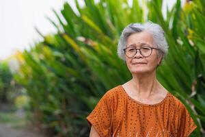 retrato de mayor mujer con corto blanco pelo en pie sonrisa y mirando a el cámara en jardín. antiguo personas sano y tener positivo pensamientos en vida hacer su contento cada día. salud cuidado concepto foto