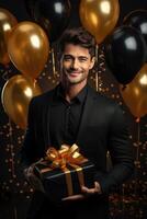 happy Caucasian birthday man holding with gift box, black and gold balloons in the background. photo