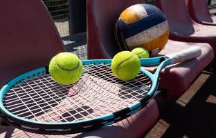 un tenis raqueta, pelotas y un vóleibol en un banco en el Deportes tribuna foto