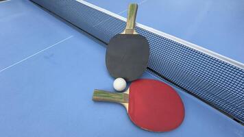 Two table tennis rackets and balls on a blue table with net. photo
