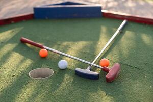 Assorted miniature golf putters and balls askew on synthetic grass. photo