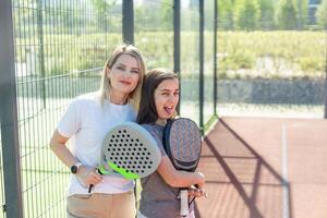 alegre entrenador enseñando niño a jugar padel tenis mientras ambos en pie en tenis Corte foto