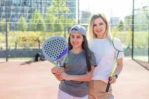 contento caucásico madre y hija jugando padel tenis y bádminton en tenis Corte al aire libre foto