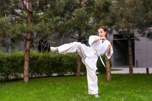 joven activo niña vistiendo en blanco kimono con blanco cinturón ejecutando marcial letras patada habilidades. deportivo kárate mujer mejorando lucha técnica en chino puente. concepto de deporte. foto