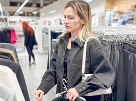 un joven mujer elige un camisa en un ropa Tienda foto