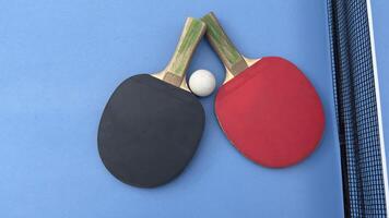 Two table tennis rackets and balls on a blue table with net. photo