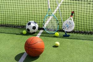 football soccer ball basketball tennis ball and racket laid on grass at sunset photo