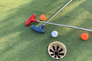 Mini-golf clubs and balls of different colors laid on artificial grass. photo