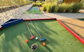 Assorted miniature golf putters and balls askew on synthetic grass. photo