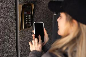 Female hand holding black mobile smart phone with smart home application on the screen. Blurred house on the background. For access to all of the controls of your house and caring of home security photo