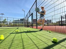 Portrait of active emotional woman playing padel tennis on open court in summer, swinging racket to return ball over net .. photo