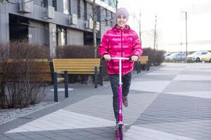 Little cute girl riding a scooter on a path in the park photo