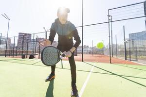 un padel jugador saltar a el pelota, bueno mirando para publicaciones y póster. hombre con negro raqueta jugando un partido en el abierto detrás el red Corte al aire libre. profesional deporte concepto con espacio para texto foto