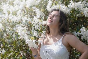 beautiful young woman wearing white summer dress surrounded by white rhododendron blossom photo