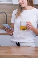 young woman making tea in the morning and using smartphone photo