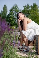 bonito joven mujer en blanco vestir sentado a el sabio flor campo. foto