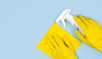 limpieza concepto. mujer manos en amarillo guantes, trapo y limpieza rociar en un azul antecedentes. de cerca. parte superior vista. Copiar espacio. foto