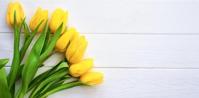 Flatlay composition with bouquet of beautiful yellow tulips on a white wooden background. Banner. Greeting card. Top view. Place for your text. photo