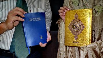 holding the bible of the new testament and the book of the quran photo