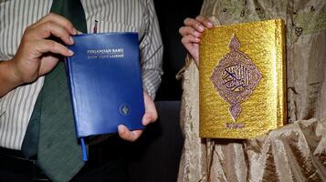 holding the bible of the new testament and the book of the quran photo