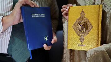 holding the bible of the new testament and the book of the quran photo