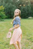 Smiling young woman in casual clothes strolls through the park. She is holding shoes in her hands. She is free and happy. The concept of freedom and youth photo